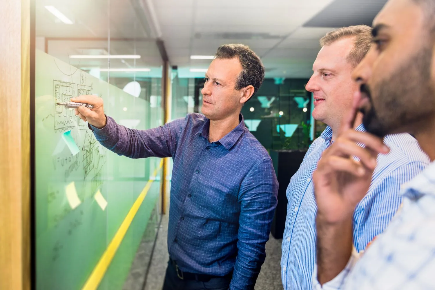 Colleagues collaborating at a glass whiteboard during a strategy session