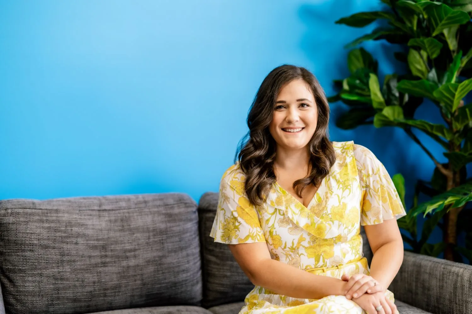 Personal branding portrait of a woman seated against a blue feature wall