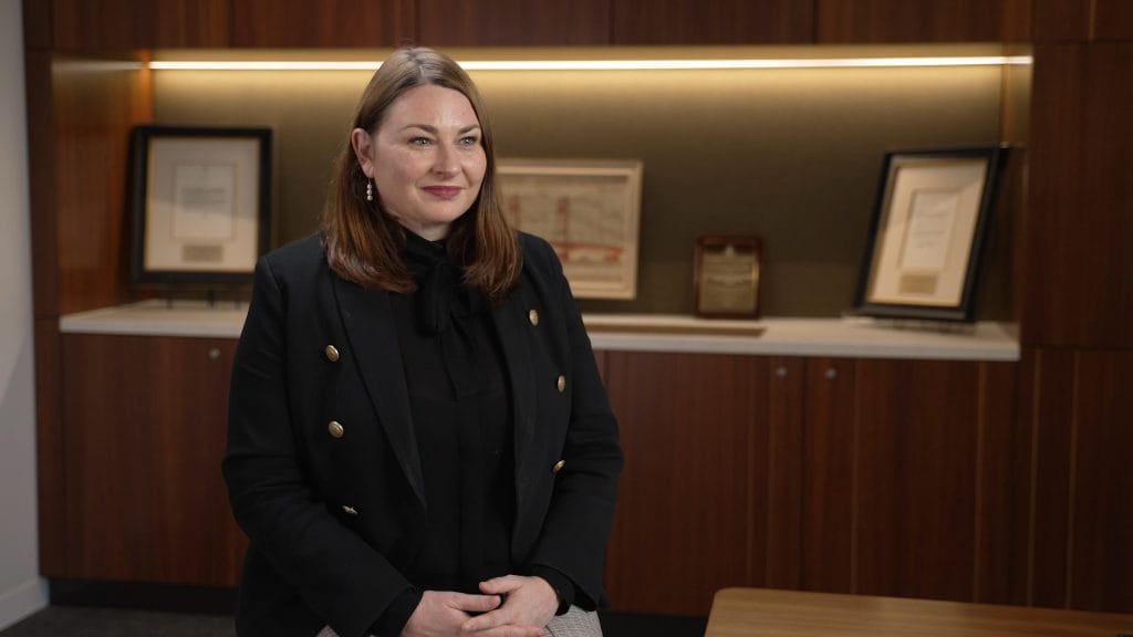 Woman in black jacket smiling in office setting.