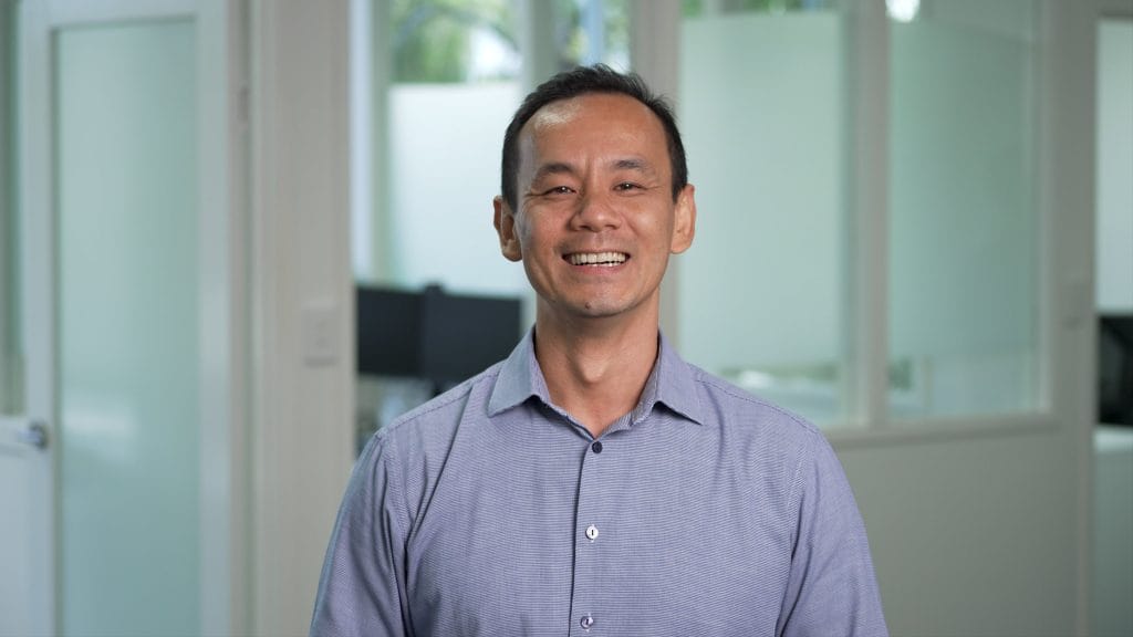 Smiling man in office wearing purple shirt.