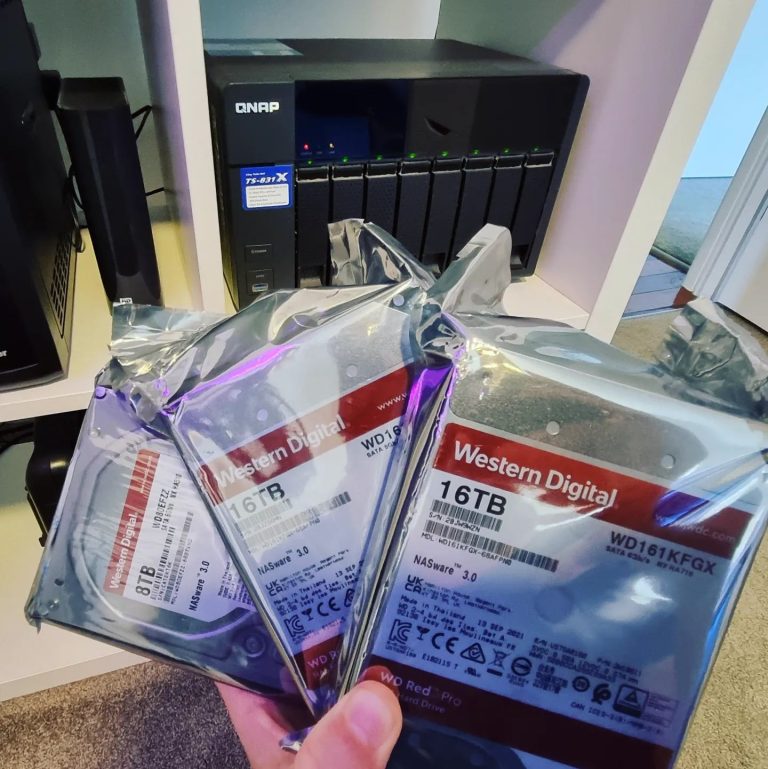 Several Western Digital RED hard-drives with a QNAP NAS in the background